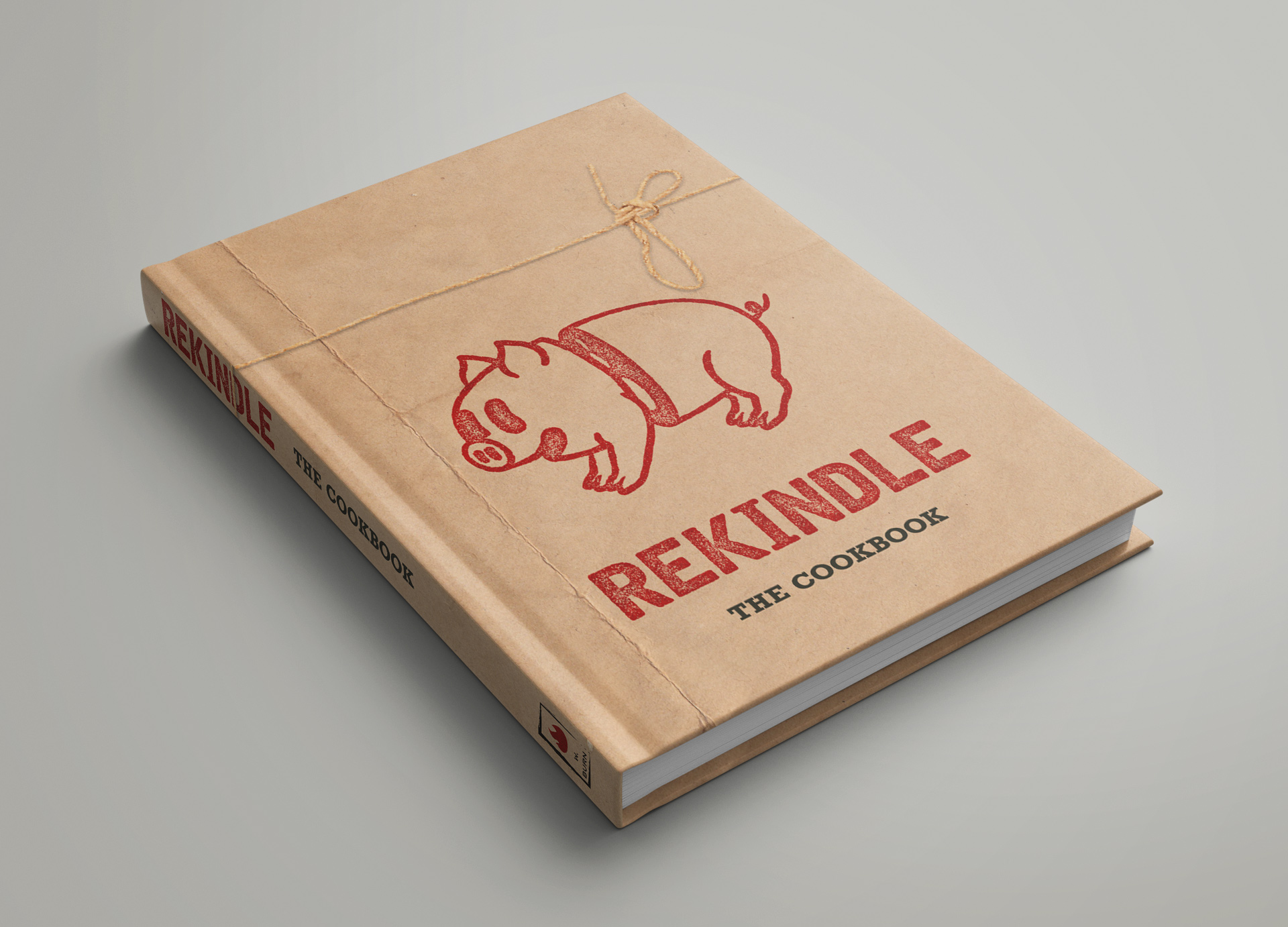 Mockup of cookbook wrapped in kraft paper and twine, with a stamp of a rubber-hose style pig, sliced in half and smiling, on the front.